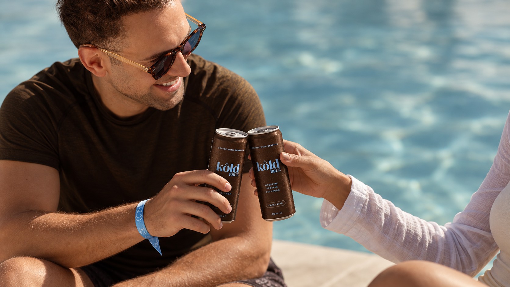 Zwei Freunde stoßen am Pool mit KôldBrue Dosen an